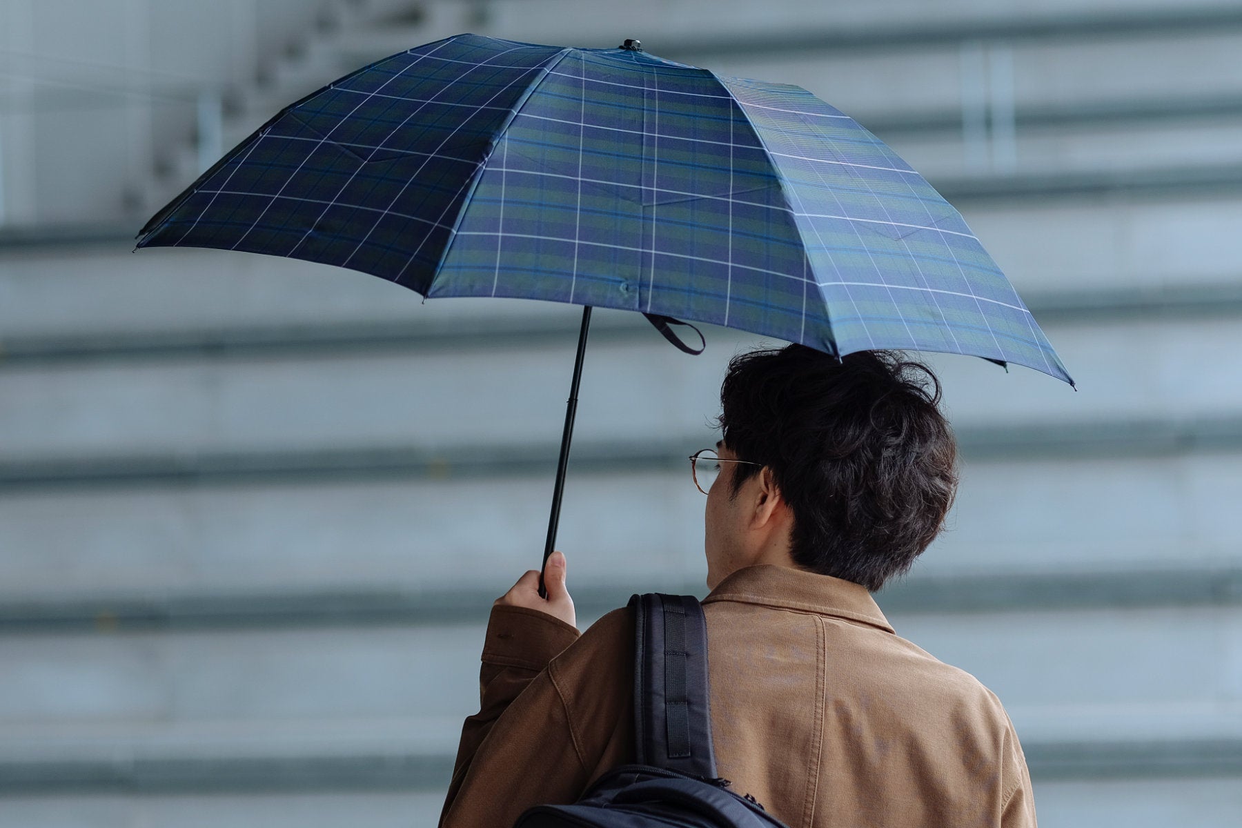 チェック柄の折りたたみ傘を差す男性