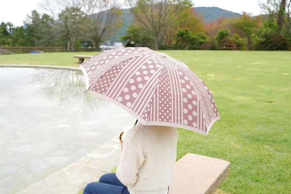 ドットとストライプ柄の折りたたみ傘を差す女性