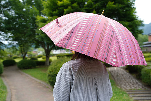 ピンク色の晴雨兼用日傘を差す女性