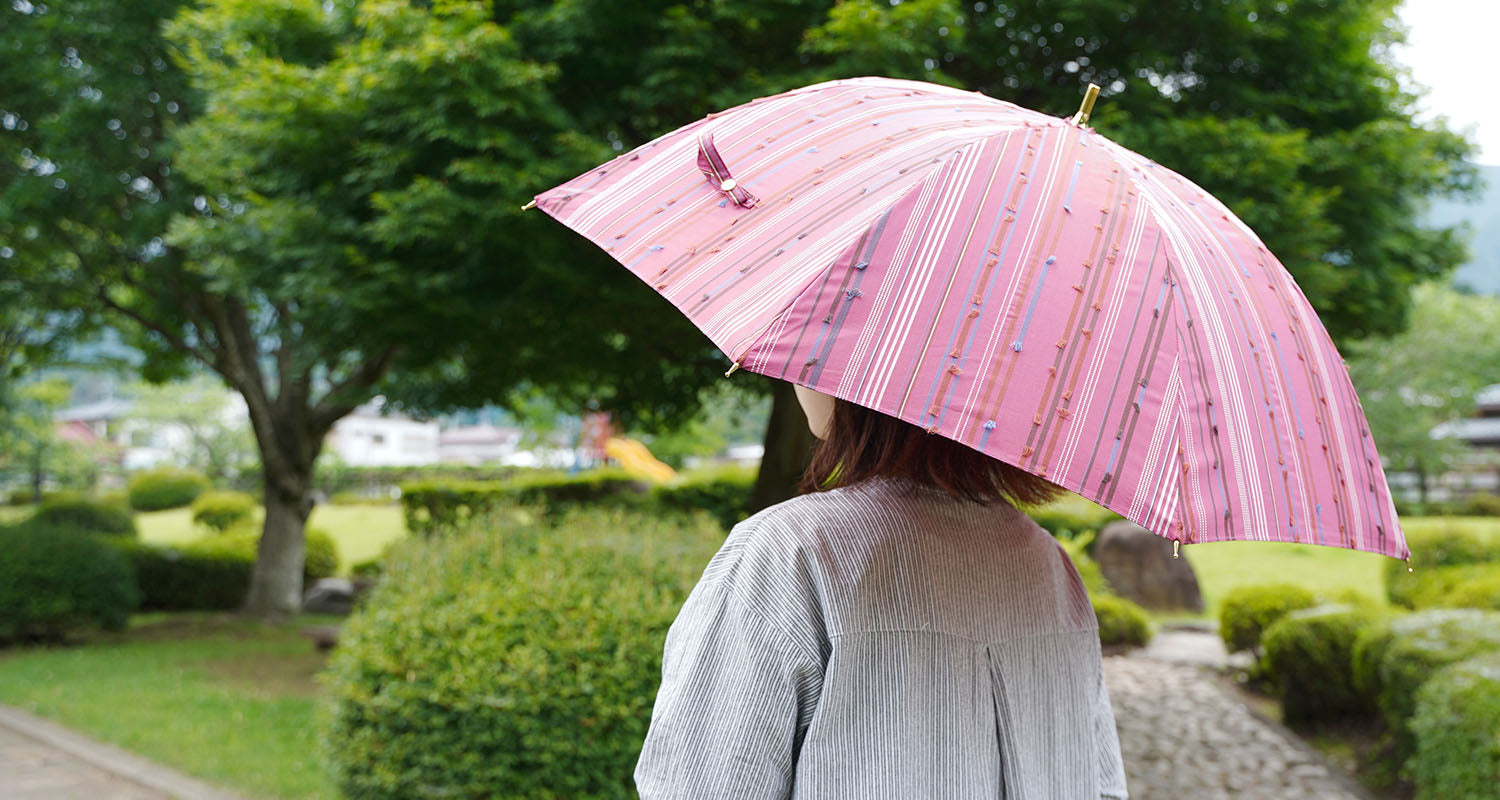 ピンク色の晴雨兼用日傘を差す女性