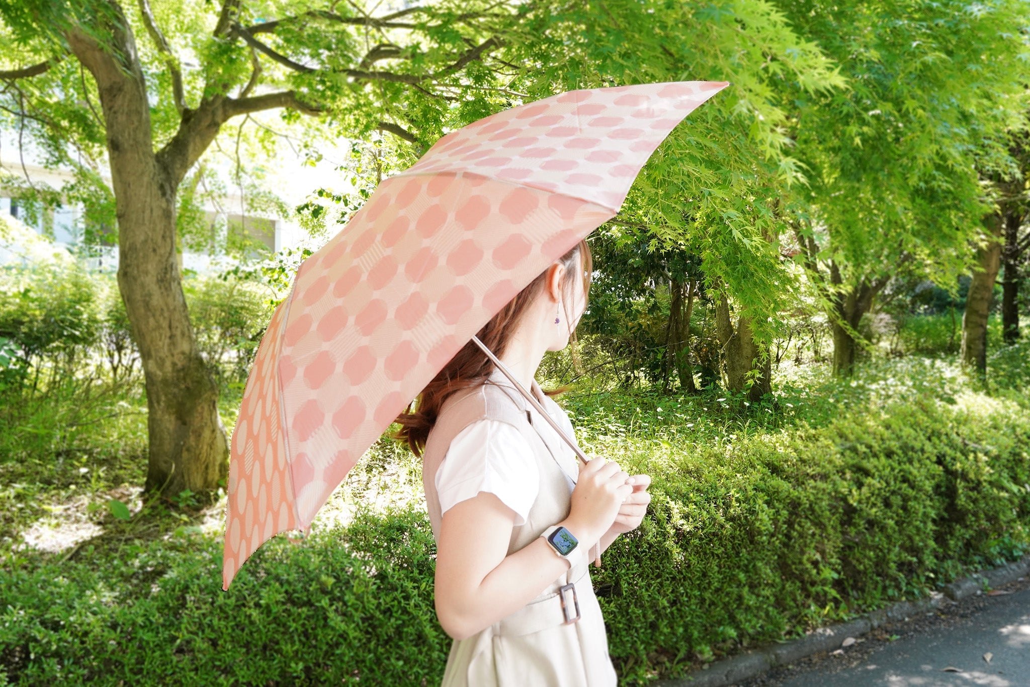 ピンクのドット柄の折りたたみ傘を差す女性