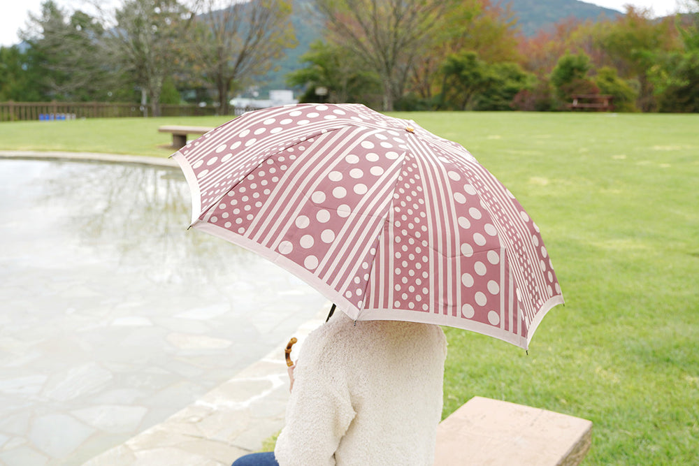 ボルドー色のドットとストライプ柄の折りたたみ傘を差す女性